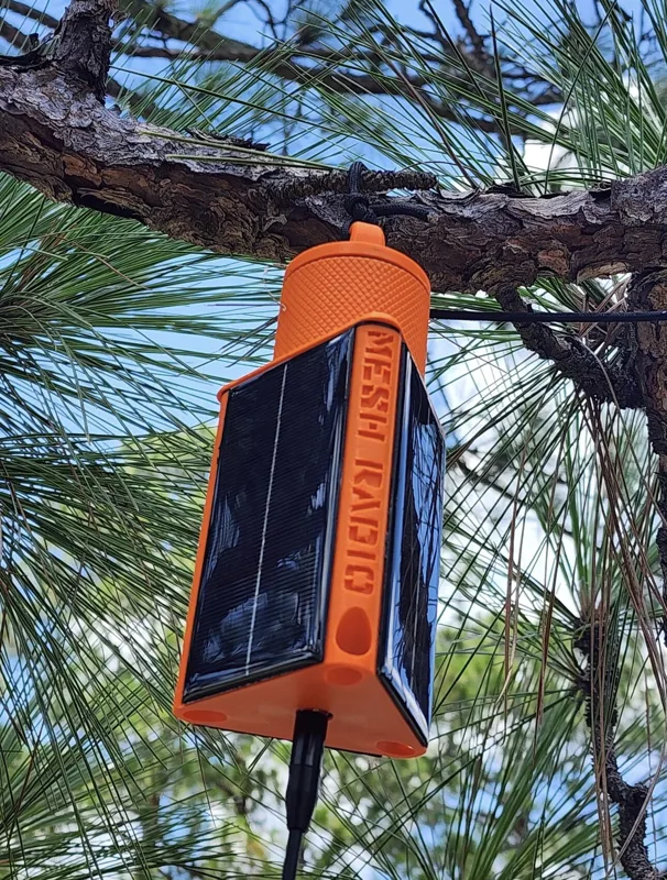 Orange 3D printed hanging Meshtastic solar node with solar panel, mounted in a pine tree